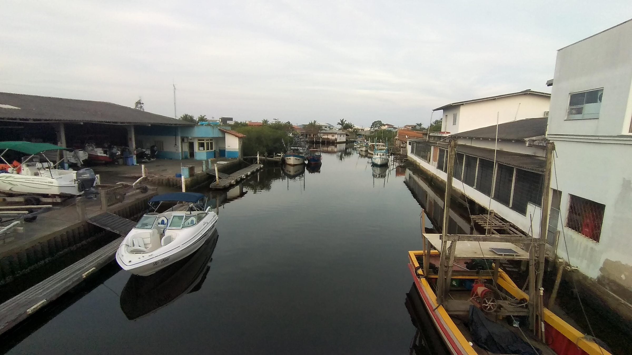 Canal que atravessa Balneário Barra do Sul, com barcos atracados junto às casas e galpões de pesca