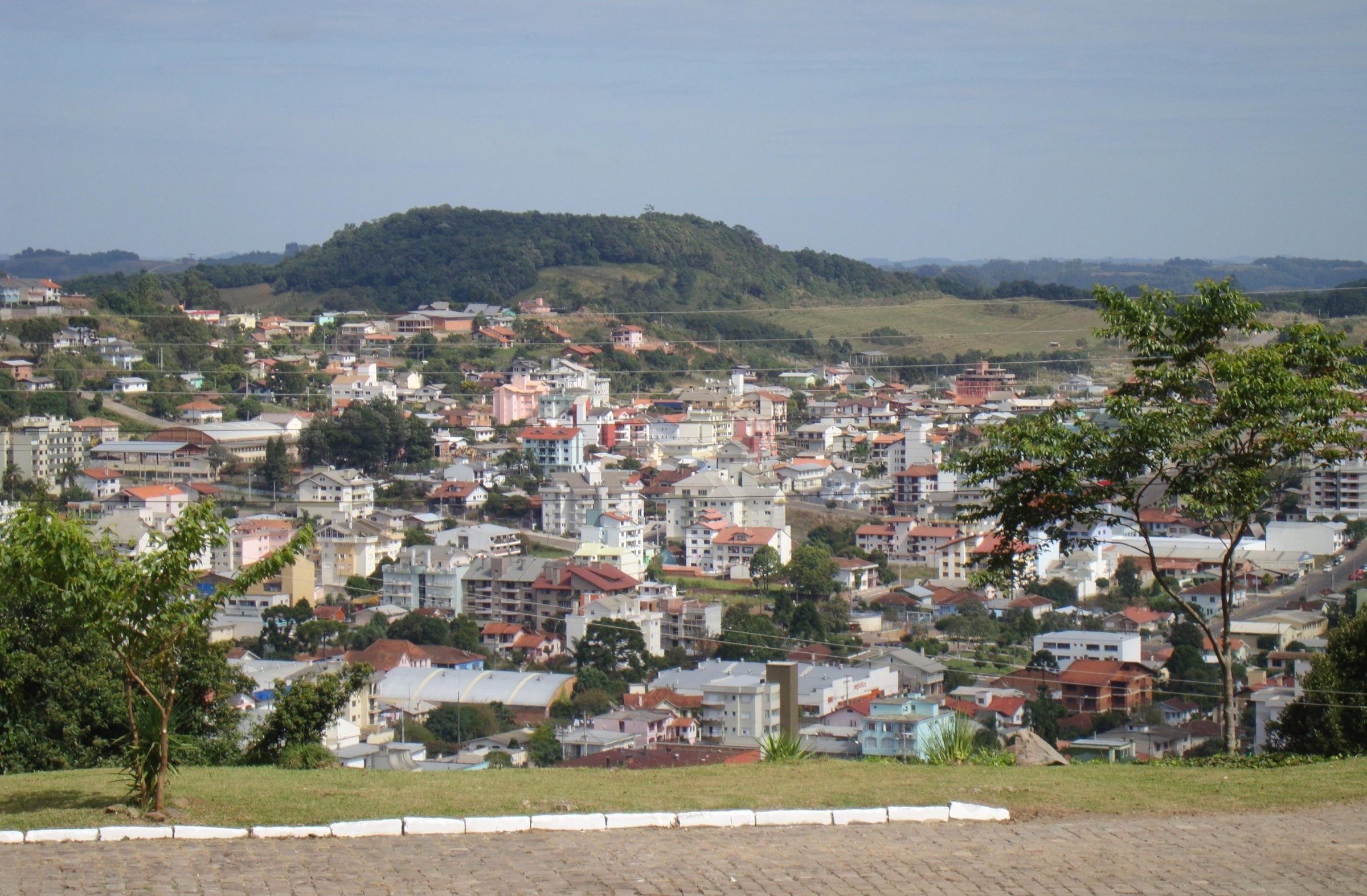 Vista panorâmica de Flores da Cunha, com as casas da cidade espalhadas pela encosta e as colinas da Serra Gaúcha ao fundo