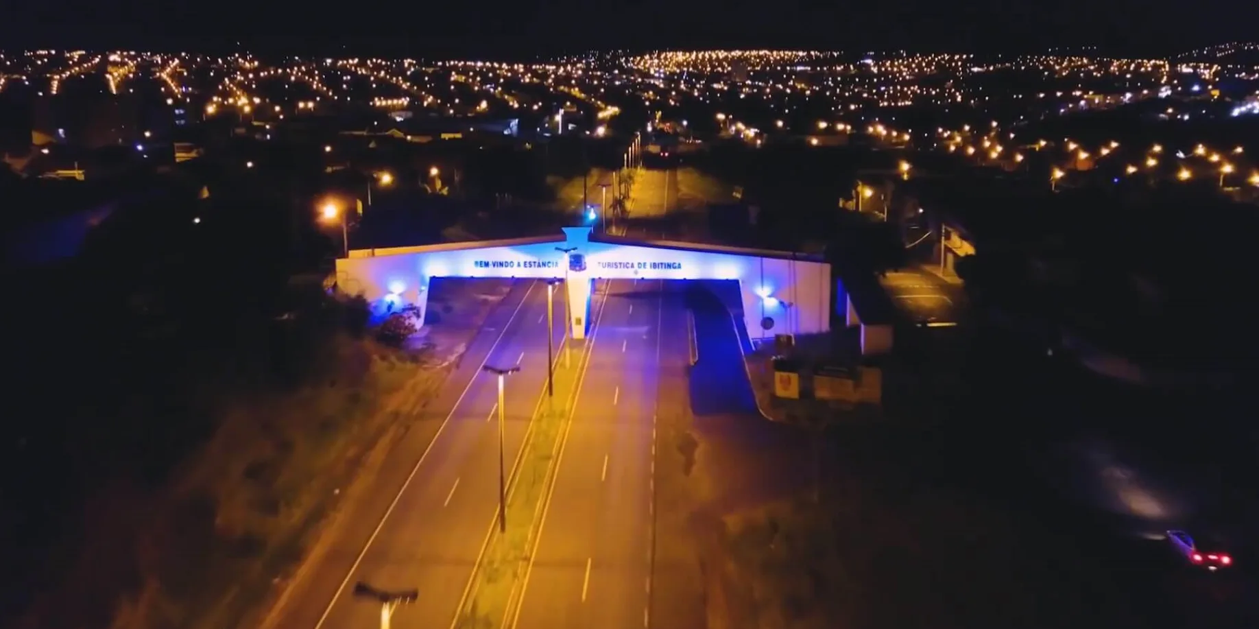 Pórtico de entrada de Ibitinga iluminado à noite, com a cidade ao fundo