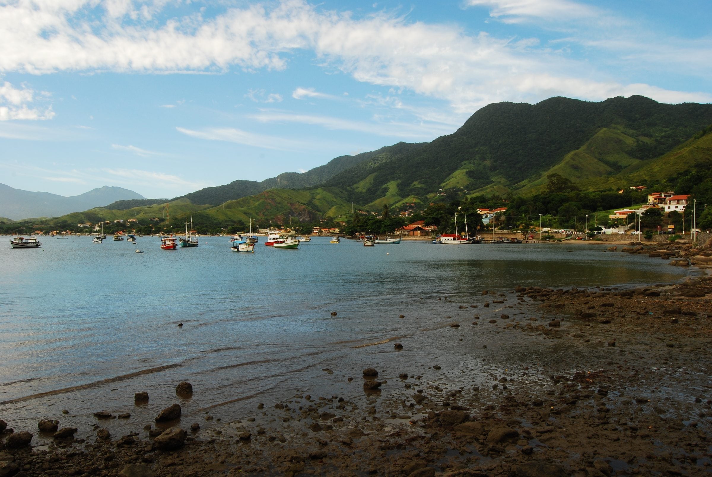 Barcos ancorados numa enseada de Ilhabela, com casas à beira-mar e os morros verdes da ilha ao fundo